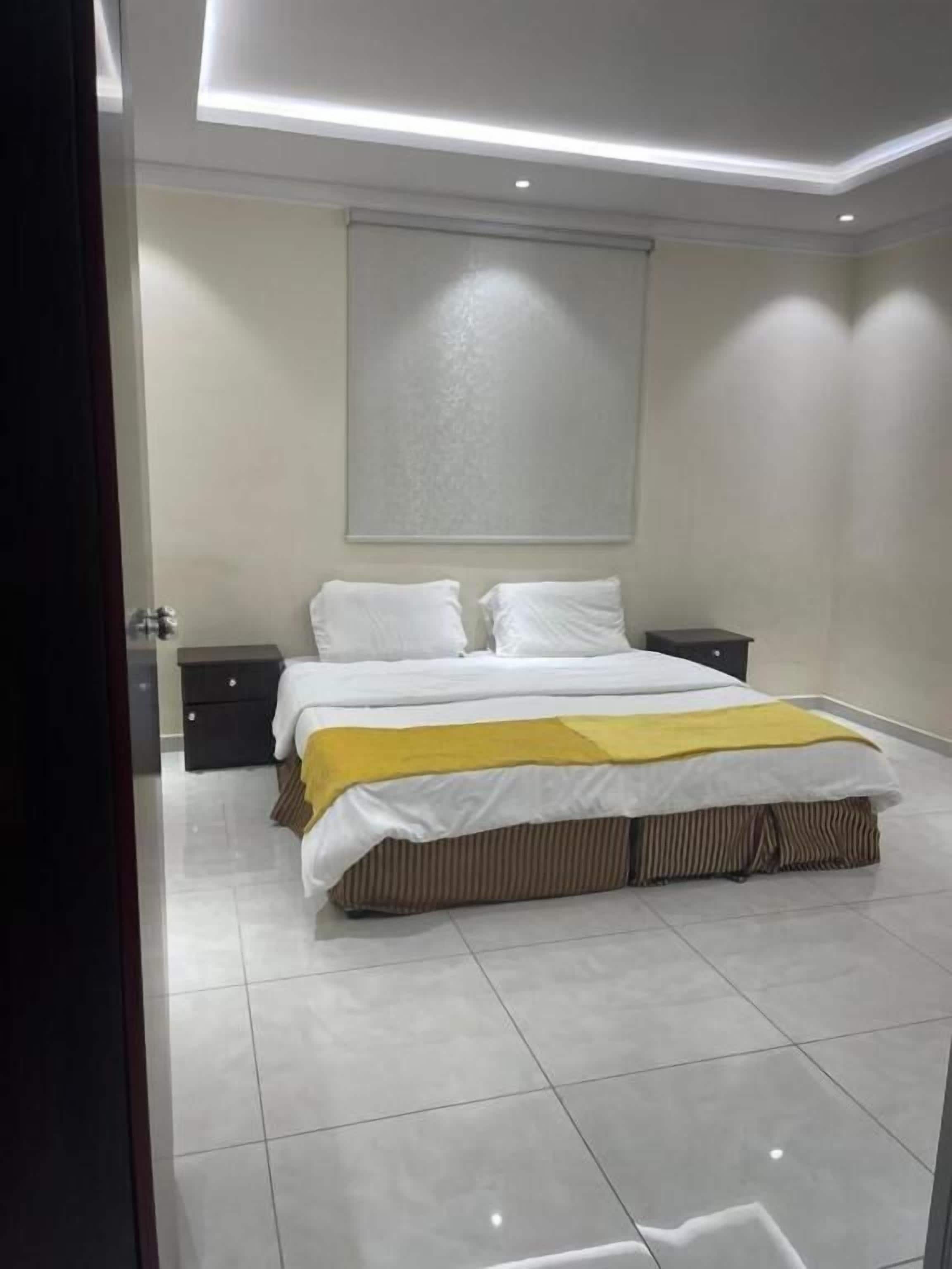 A bedroom with a bed, nightstands, a headboard, and a large window.