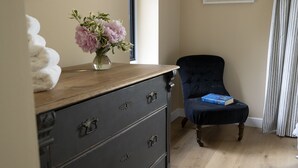 Una habitación con un aparador de madera, una silla, un libro y un jarrón con flores.