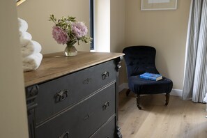 Ein Zimmer mit einem Holzkasten, einem Stuhl, einem Buch und einer Blumenvase.