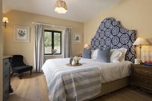 Ein Schlafzimmer mit einem Bett, einem Sessel, einem Nachttisch, einer Lampe und einem Fenster mit Vorhängen.