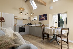 Eine gemütliche Küche mit Essbereich, Holzbalken, einem eingebauten Backofen und einem großen Fenster mit Vorhängen.