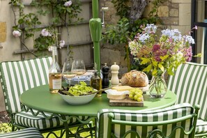 Ein runder Tisch mit einer Flasche Cotes de Provence Wein, zwei Gläsern, einer Salatschüssel, einem Brotlaib, einer Käseplatte, einer Vase mit Blumen und einem Gewürzmühle.