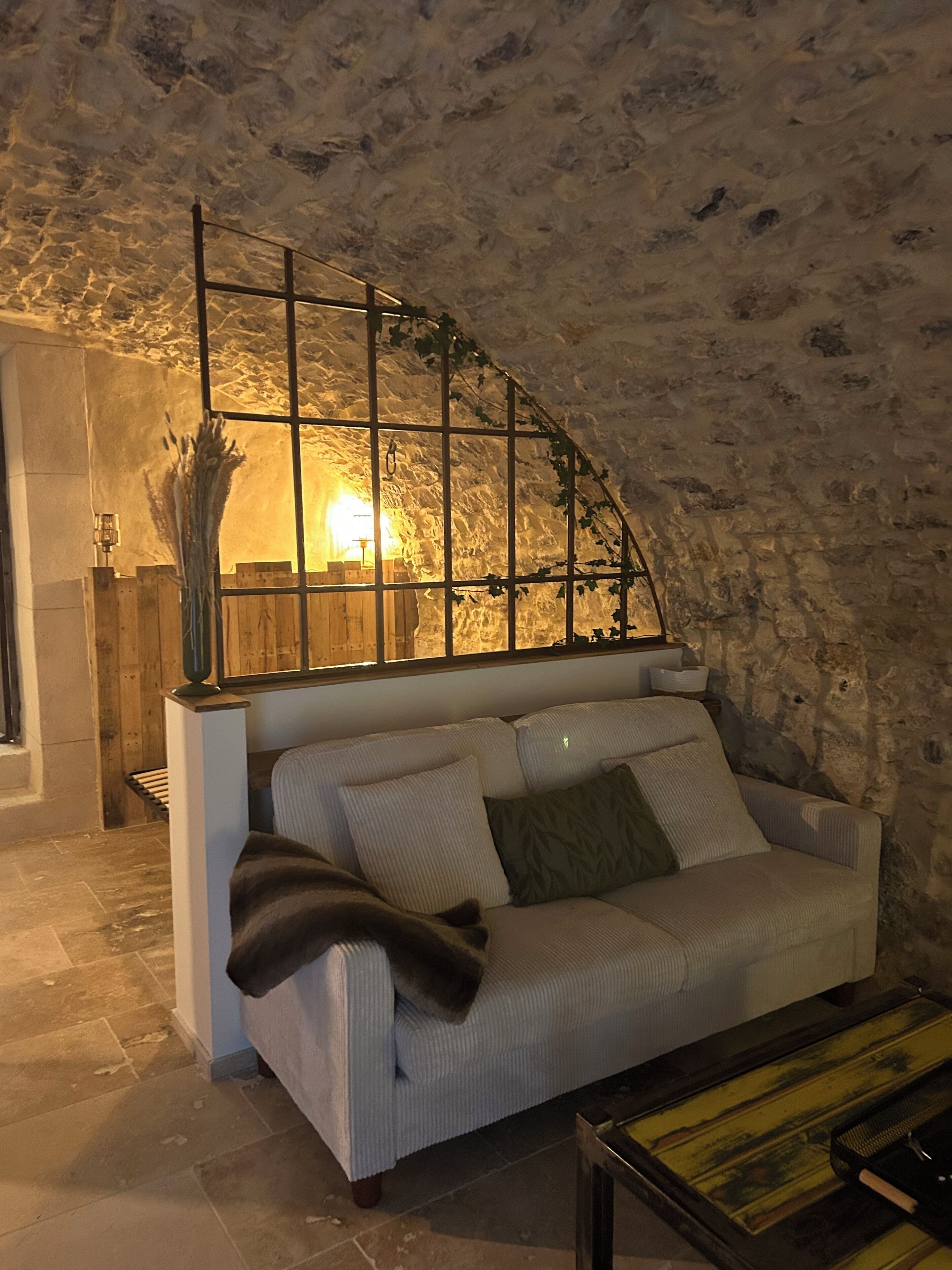 Un intérieur chaleureux avec un mur en pierre, un banc en bois, un canapé confortable et une table sur laquelle se trouve un plateau.