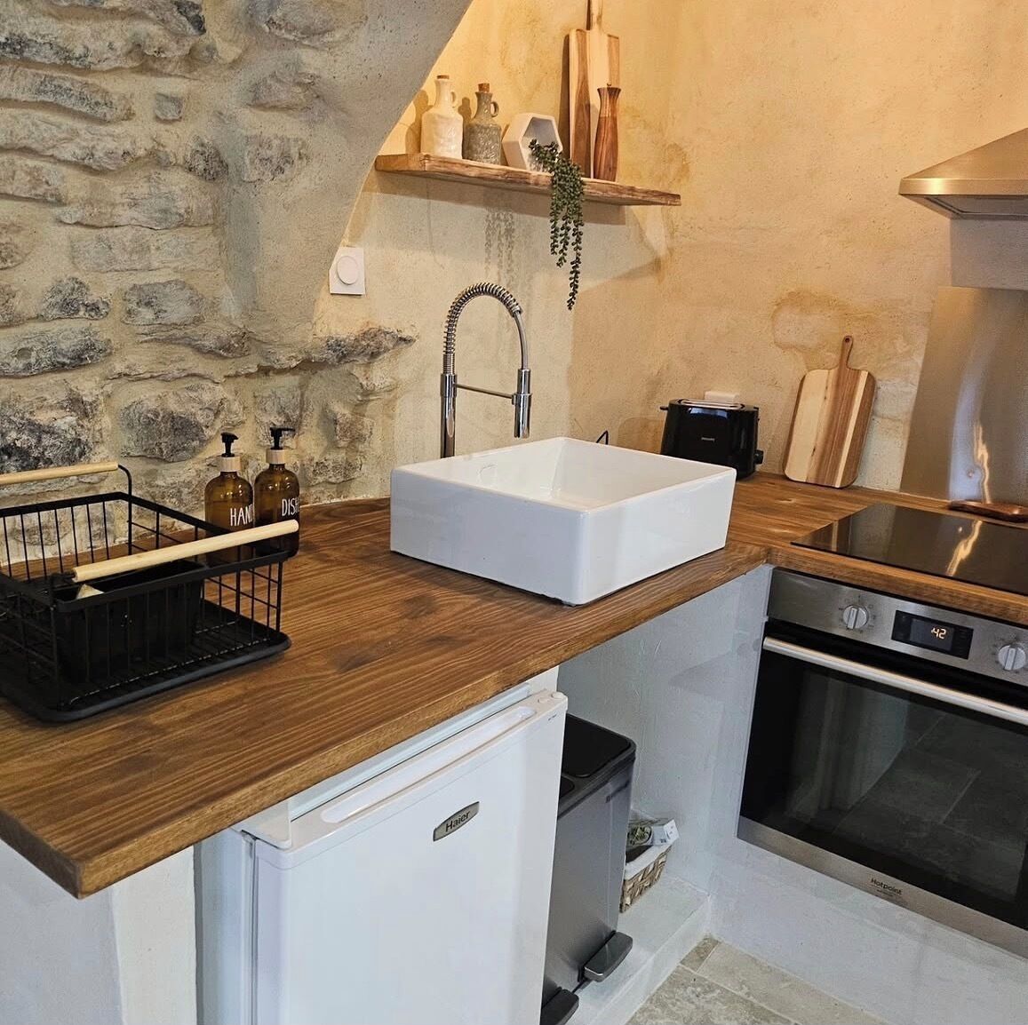A compact kitchen with a white sink, wooden countertop, a small refrigerator, and a built-in oven.