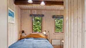 Ein Schlafzimmer mit Holzwänden, einem Bett, zwei Fenstern und einer Heizung.
