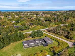 Un quartier résidentiel où les maisons sont entourées de verdure et où une route mène à la mer.