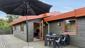 Eine Holzterrasse mit Tisch, Stühlen und Sonnenschirm, sowie ein Gebäude mit rotem Dach.