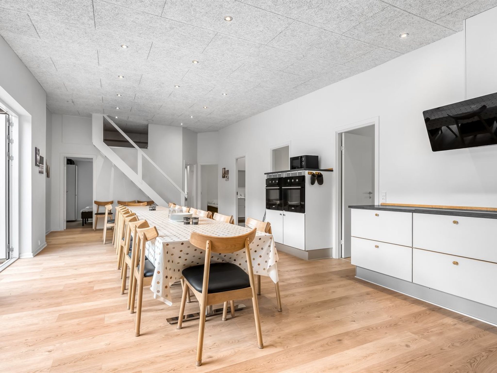A modern kitchen with white cabinetry, a wooden dining table with chairs, and a staircase leading to another level.