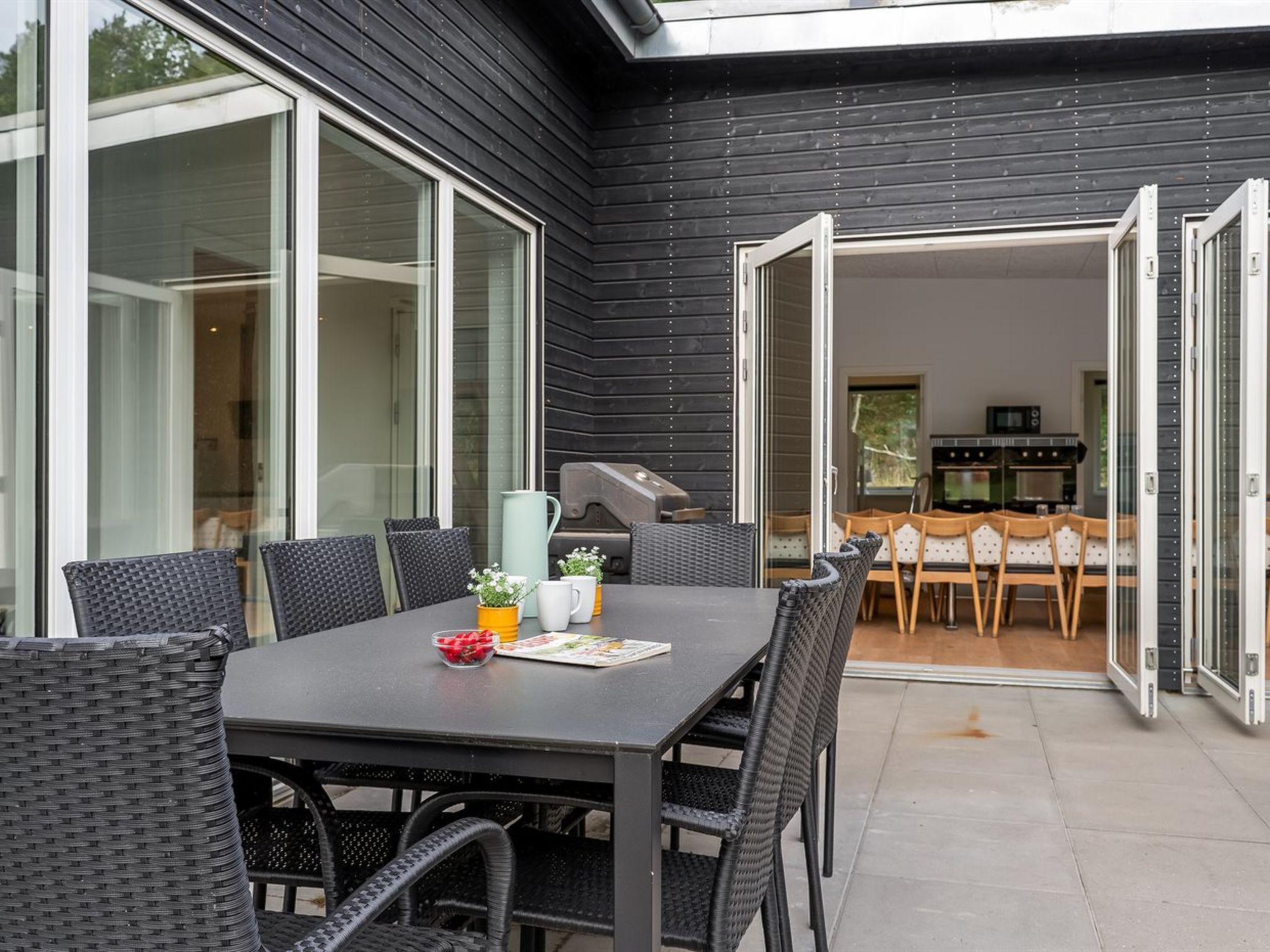 An outdoor patio with a table and chairs, a grill, and a view into the house.