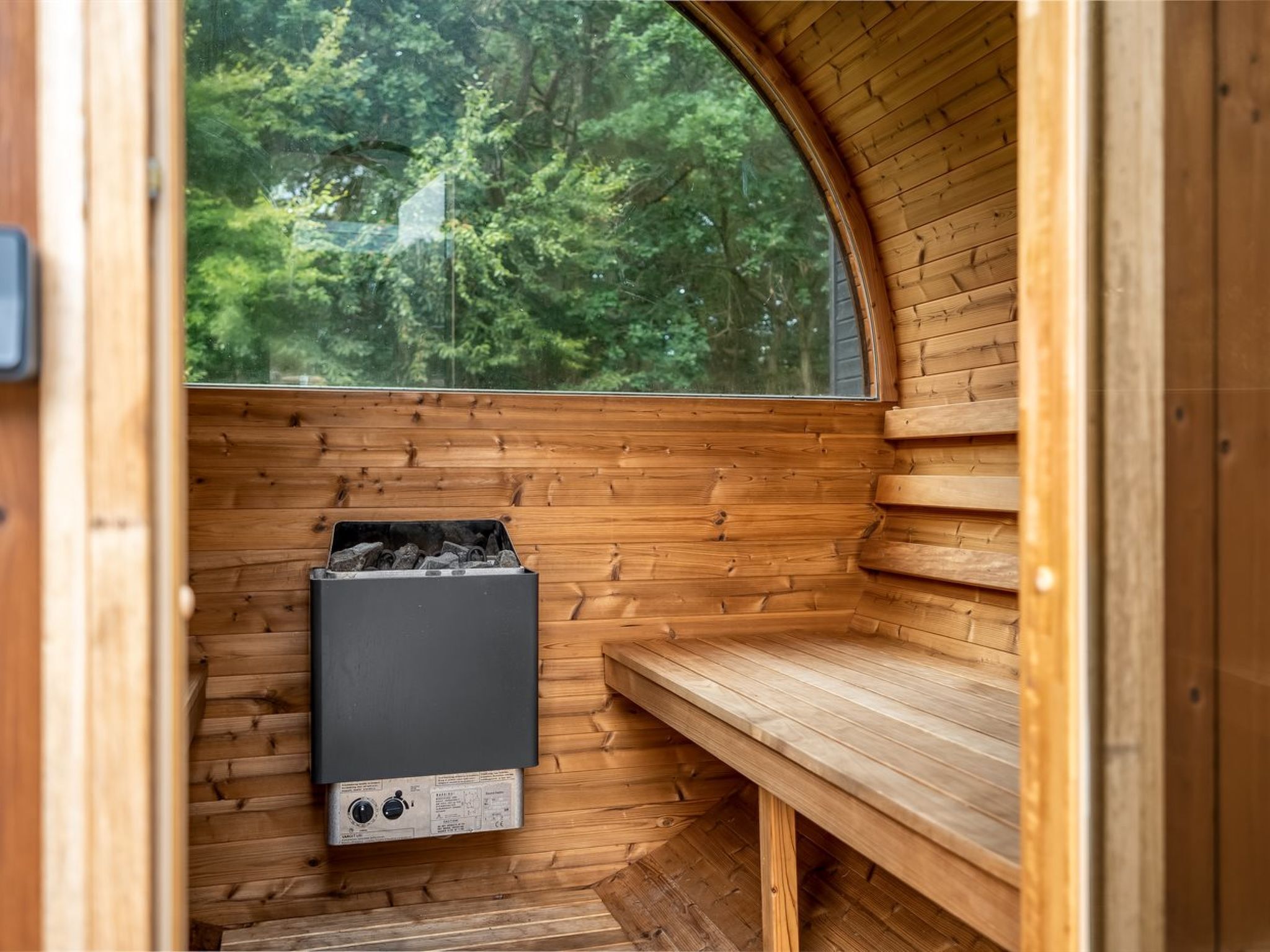 A wooden cabin interior with a bench, a fireplace, and a window overlooking a forest.
