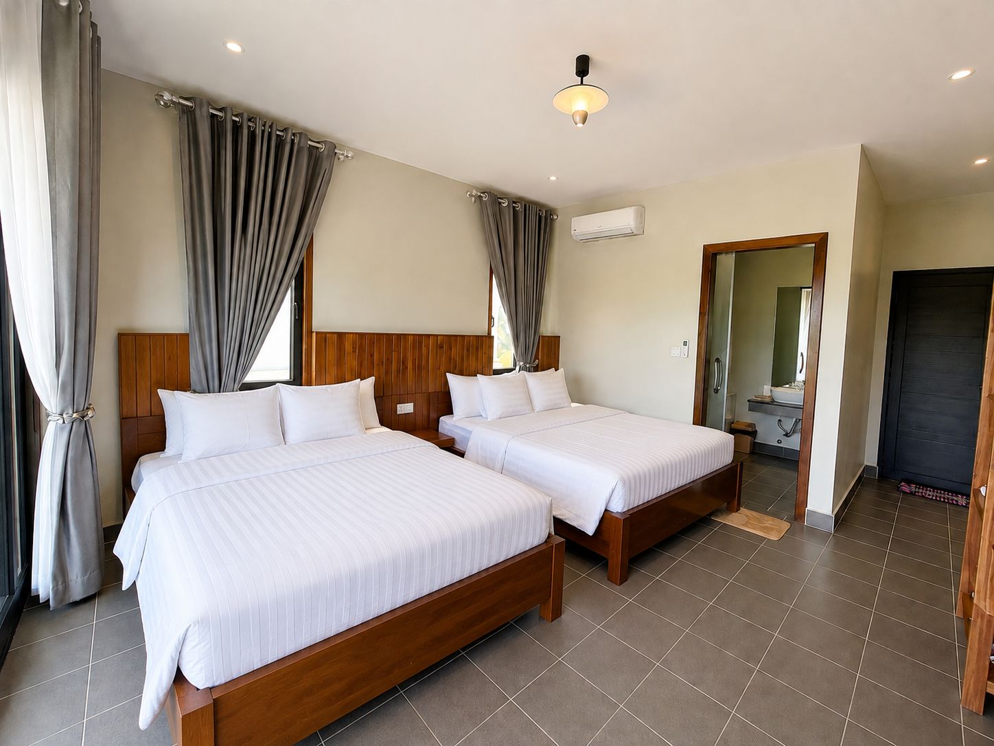 Een hotelkamer met twee bedden, een houten hoofdbord, een plafondlamp, een airconditioningsysteem en een badkamer die door een open deur zichtbaar is.