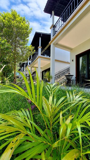 Un edificio de varios pisos con balcones, un área de jardín con plantas tropicales y un cielo despejado.