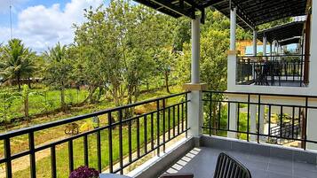 An outdoor patio with a round table and two chairs, a pergola overhead, and a view of a green landscape.