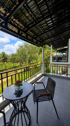 An outdoor patio with a round table and two chairs, a pergola overhead, and a view of a green landscape.