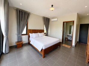 Una habitación de hotel con una cama grande, una mesita de noche, un equipo de aire acondicionado y un espejo.