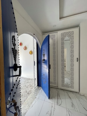 A hallway with a blue door, white walls, and a tiled floor.