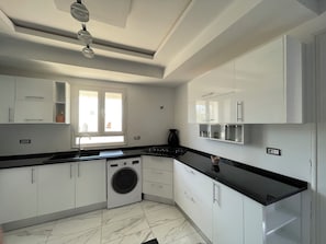 A modern kitchen with white cabinets, a black countertop, a built-in washing machine, and a window with natural light.