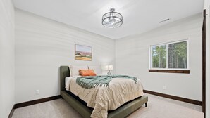 Een slaapkamer met een bed, een raam, een plafondventilator en een aan de muur bevestigd schilderij.