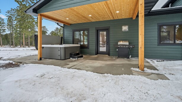 Een overdekt buitengebied met een hottub, barbecue en een betonnen terras.