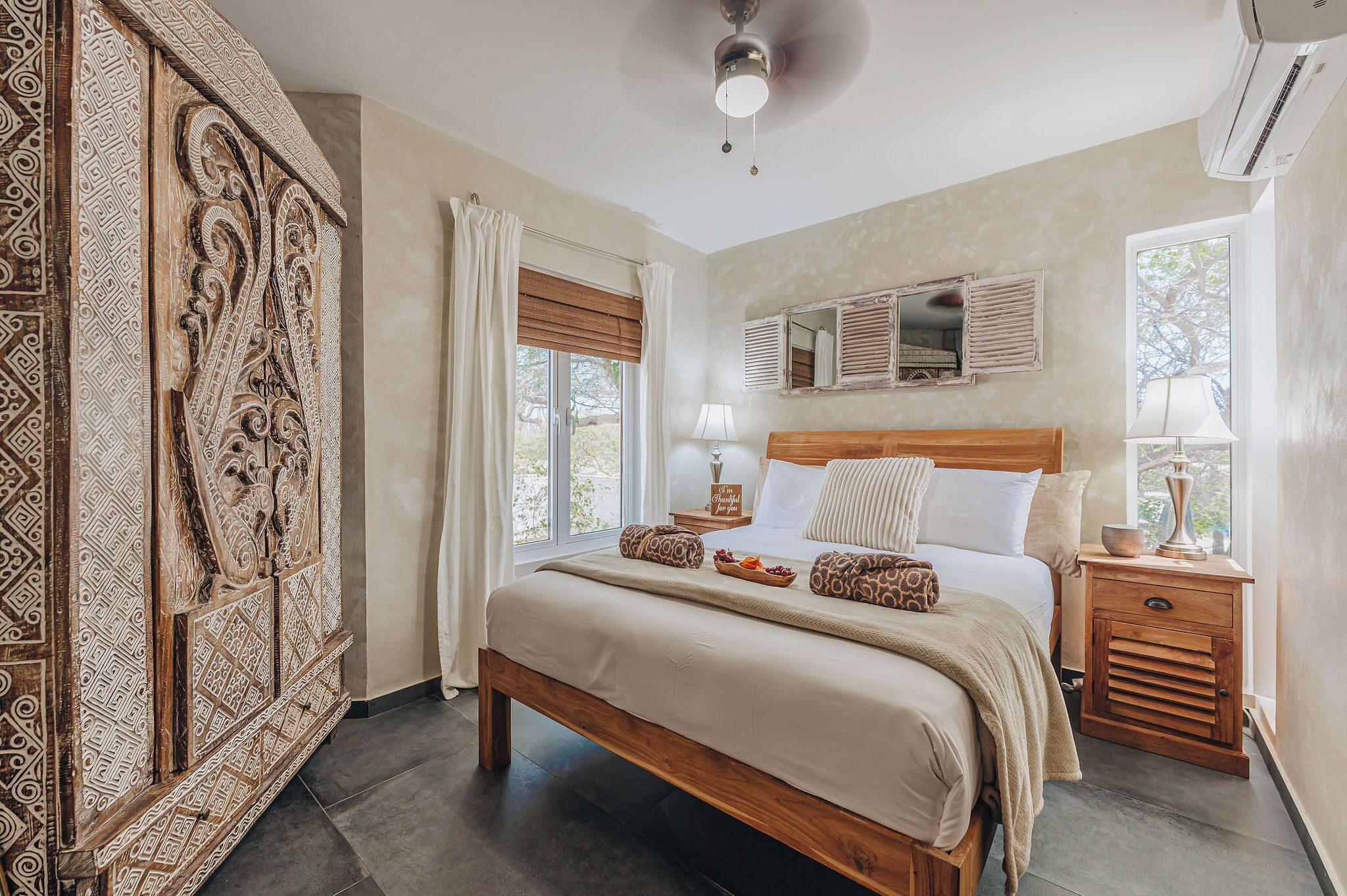 Une chambre à coucher avec un grand lit, des tables de chevet, un ventilateur de plafond et un panneau décoratif mural.