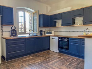 Eine moderne Küche mit dunkelblauen Schränken, einer Holz Arbeitsplatte, einem Geschirrspüler, einem Ofen und einem Fenster mit Blick auf Bäume.