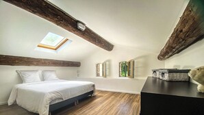 Quarto com cama, piso de madeira, claraboia e vigas de madeira no teto.