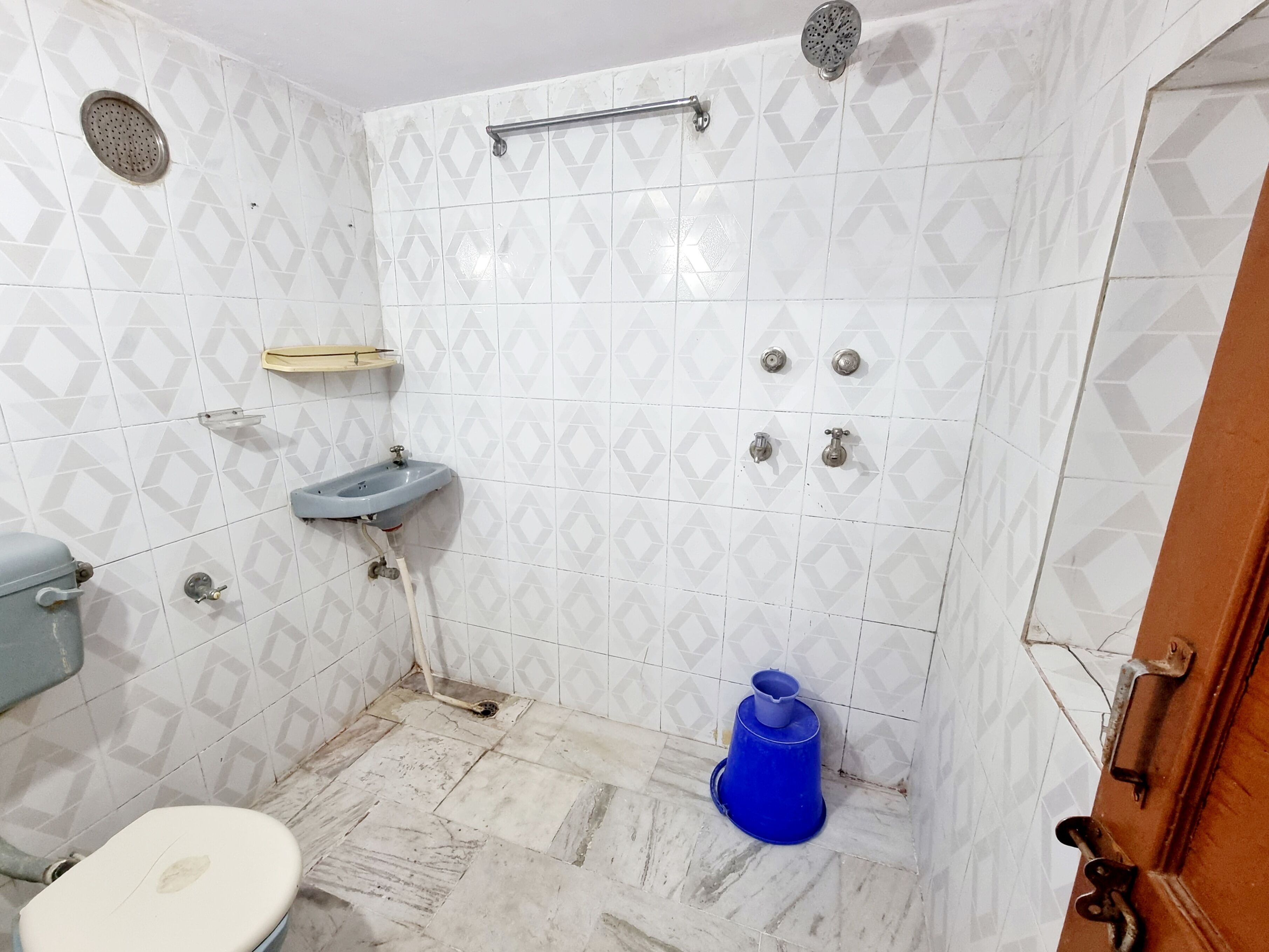 Un baño con inodoro, lavamanos, ducha y un cubo azul.