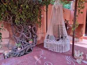 A macramé hanging chair with cushions, a macramé canopy, and a wall with climbing plants.