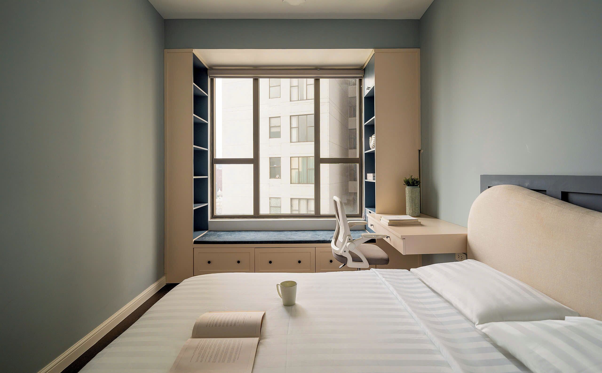 Quarto de hotel com cama, mesa de cabeceira e janela com vista para edifícios.