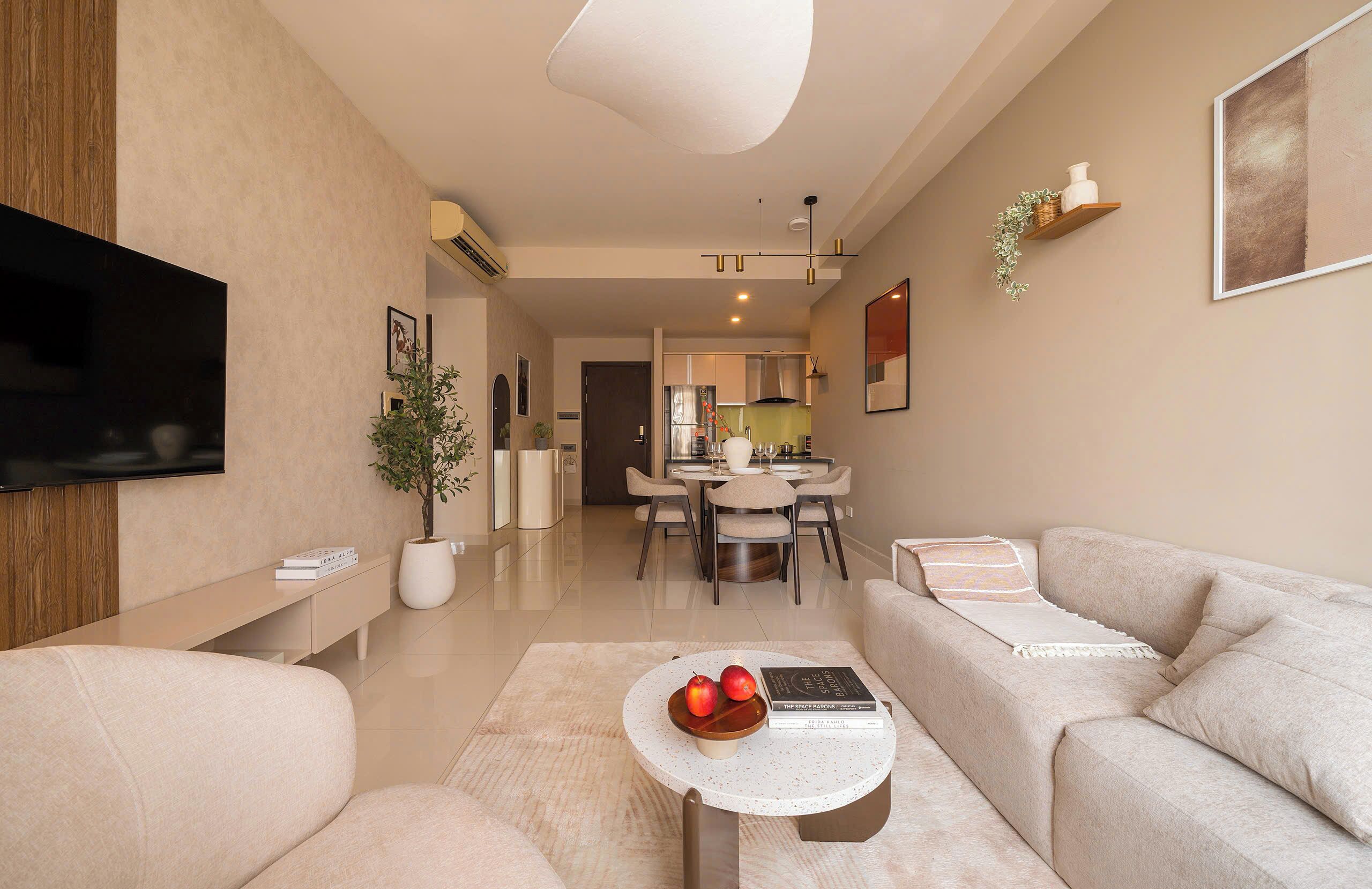 Una sala moderna con un sofá, una mesa de centro con manzanas y un libro, un televisor y un comedor al fondo.