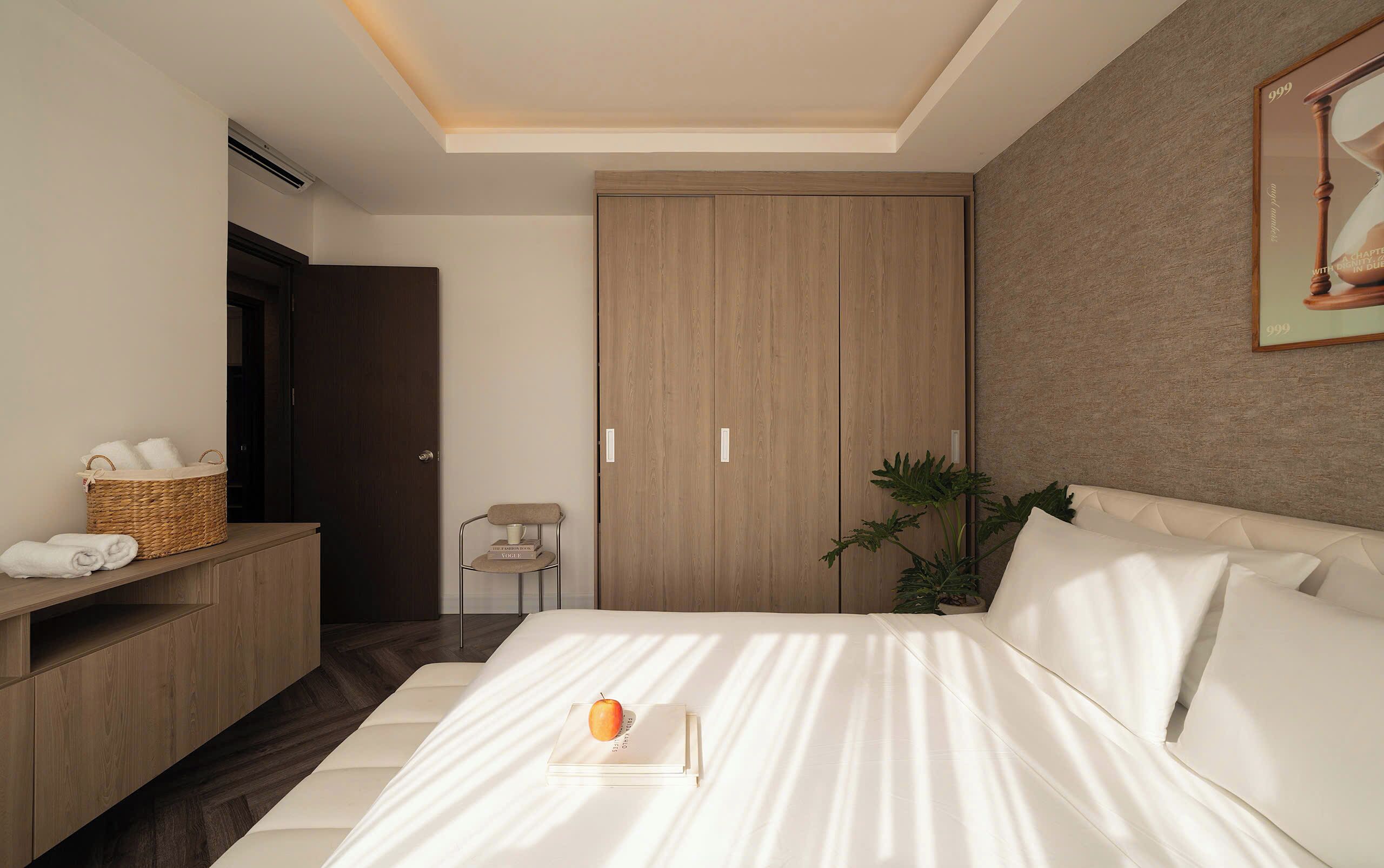Une chambre d’hôtel moderne, équipée d’un lit, d’une armoire en bois, d’un bureau avec un panier, d’une chaise et d’une plante en pot.