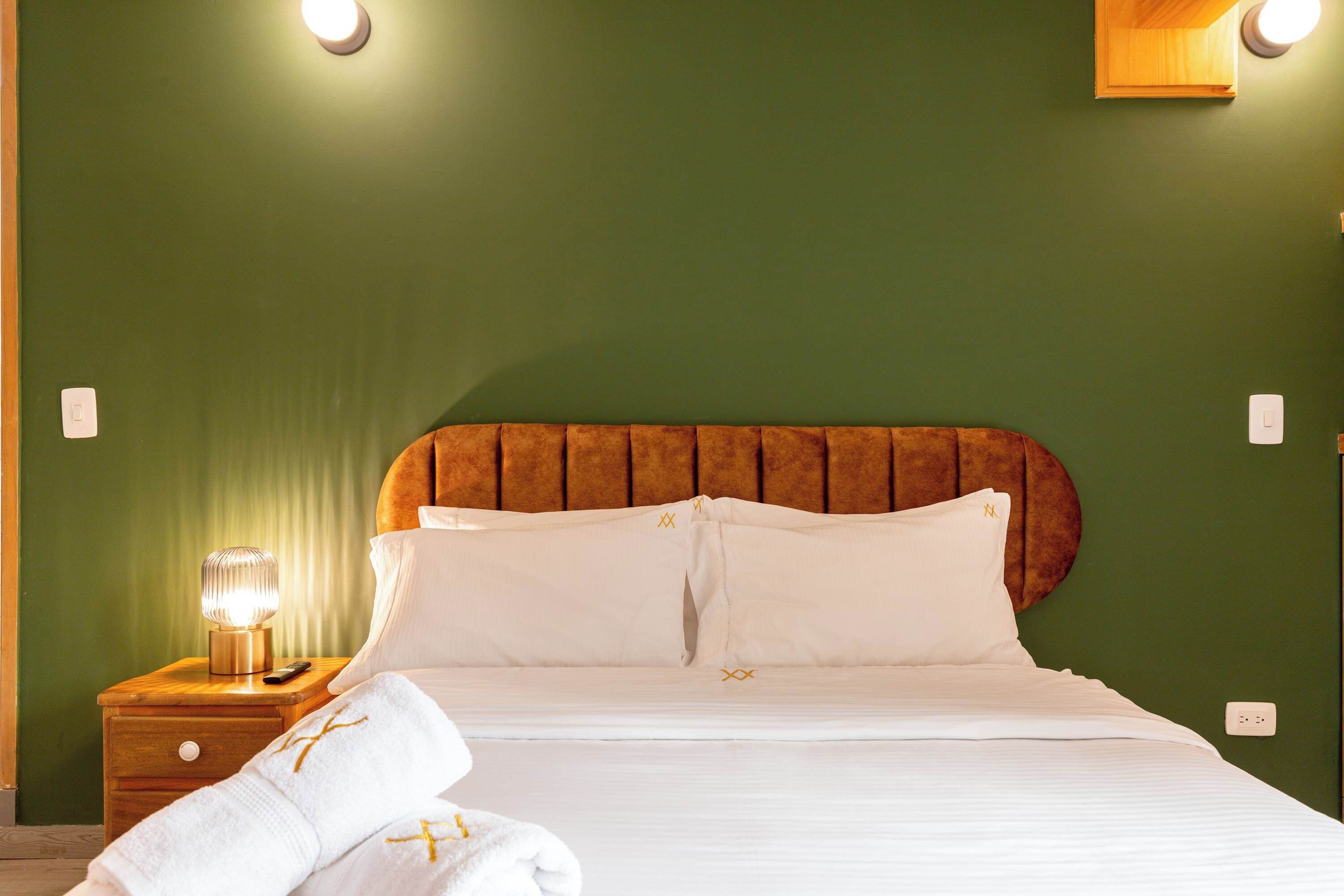 Een hotelkamer met een bed, nachtkastje, lamp en handdoeken.