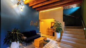 Una sala de estar moderna con una pared azul, un sofá oscuro, una mesita de centro y una escalera que lleva a un nivel superior.