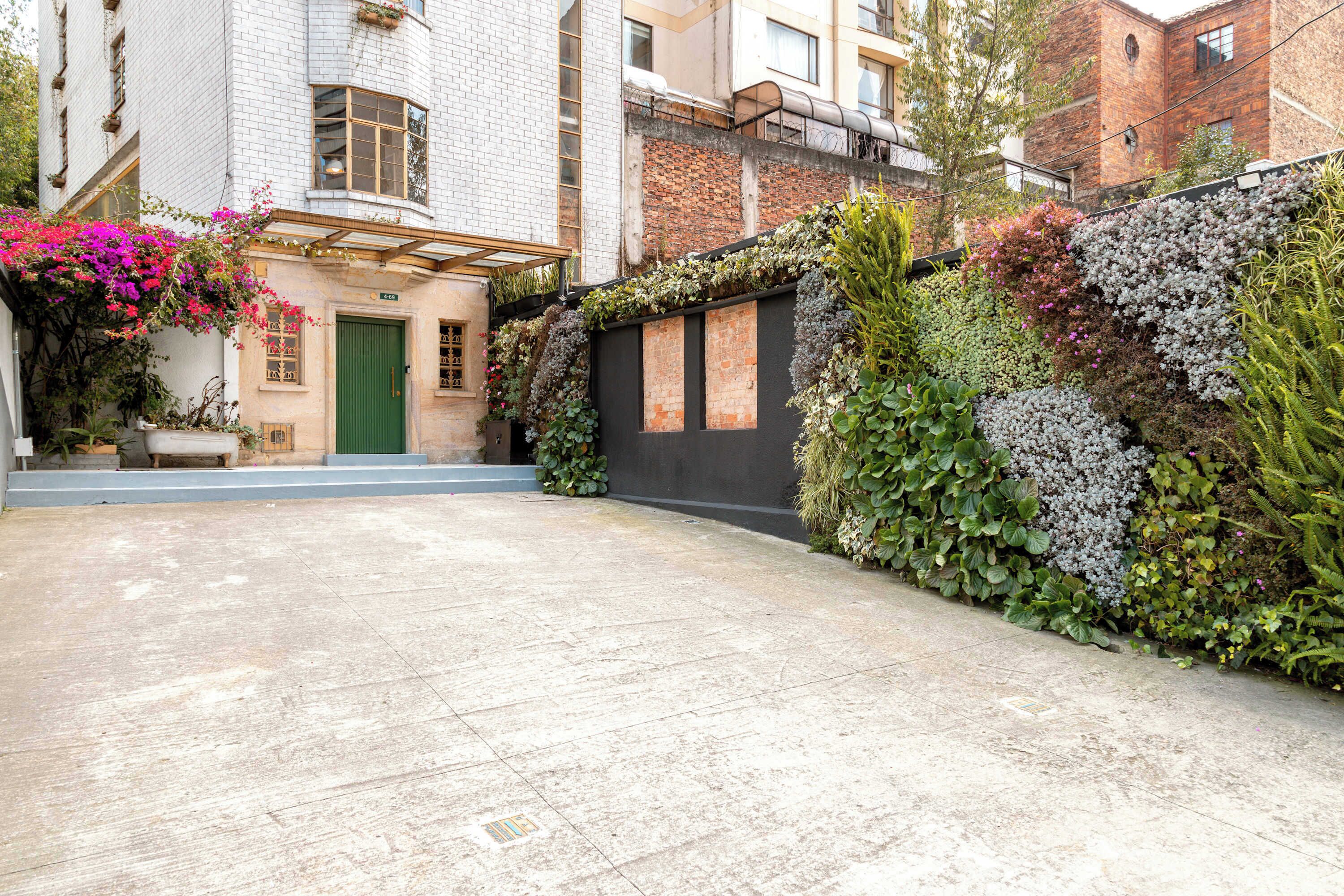 Une cour avec une porte verte, un mur de briques recouvert de plantes grimpantes et un sol pavé.