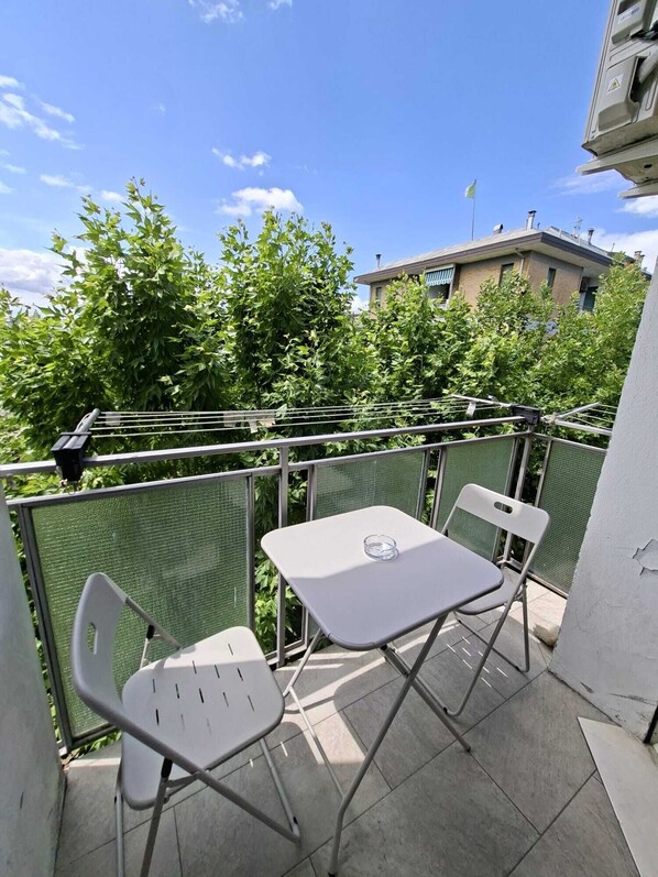 Ein Balkon mit Tisch und zwei Stühlen, umgeben von einem Metallgeländer und Pflanzen.