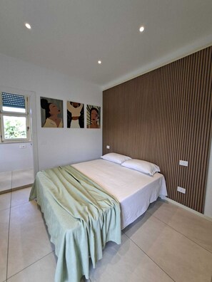 A bedroom with a bed, a window, and a wall with vertical wooden slats. - Charming studio apartment just 100 meters from the beach! (Cesenatico)