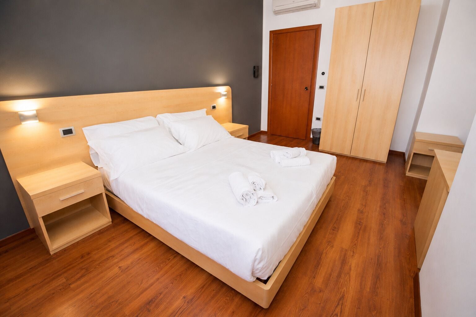 Une chambre d’hôtel avec un lit en bois, des tables de chevet, une armoire et un climatiseur fixé au mur.