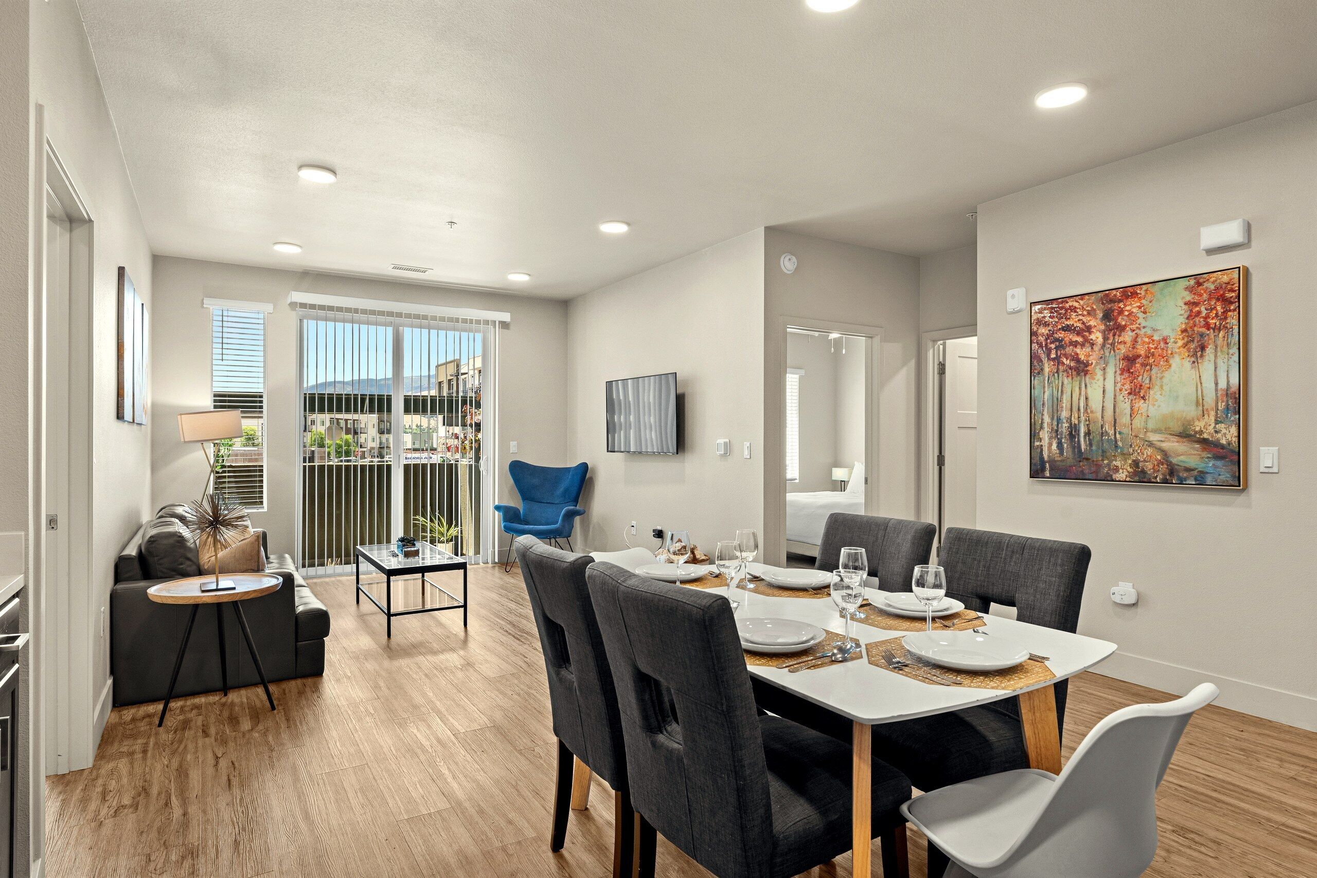 Quarto de hotel moderno com área de jantar, sofá, televisão e um quadro na parede.