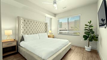 A bedroom with a tufted headboard, a single bed, a nightstand with a lamp, a potted plant, and a ceiling fan.