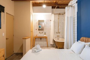 Ein Hotelzimmer mit Bett, einem Holznachttisch, einem Badezimmer mit Badewanne und Dusche.