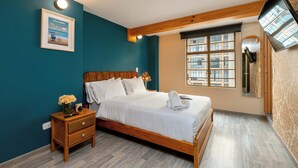 Una camera da letto con un letto in legno, un comodino, un vaso di fiori, un quadro incorniciato e una finestra con vista sugli edifici.