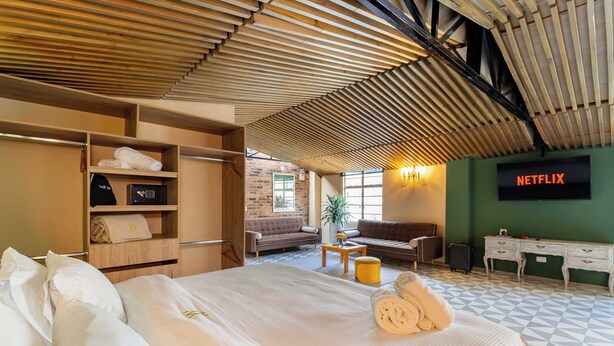 A hotel room with a bed, a sofa, a desk, and a wall-mounted TV screen displaying 'NETFLIX'. - w Unique Loft in The Heart of La Candelaria (Bogotá)