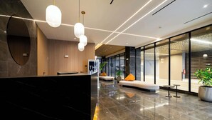 A modern lobby with a reception desk, seating area, and large windows.