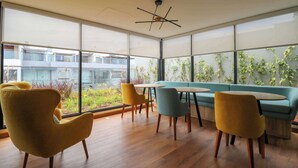 Een modern interieur met grote ramen, houten vloeren en een combinatie van gele en blauwe stoelen rondom een centrale tafel.