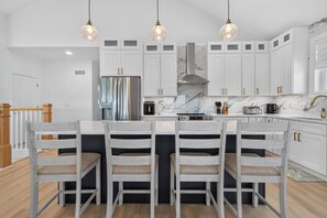 A modern kitchen with white cabinets, a marble backsplash, and a central island with four chairs. - Brand NEW Boaters Dream in Slaughter Beach (Milford)