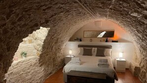 Une chambre à coucher avec un plafond en pierre, un lit avec des oreillers, une table de chevet et une commode.