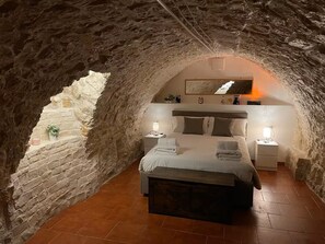 A bedroom with a stone ceiling, a bed with pillows, a bedside table, and a nightstand.