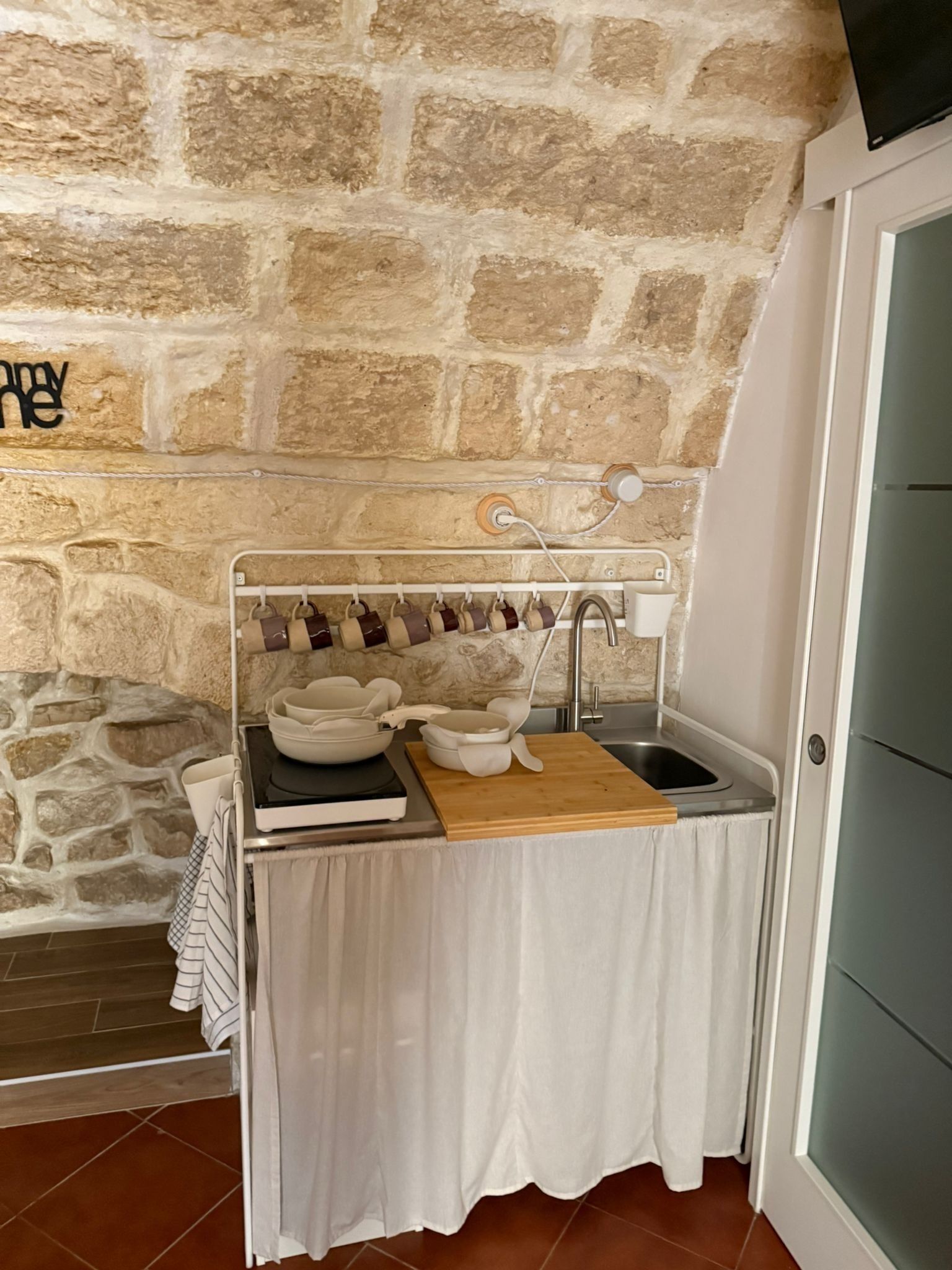 A compact kitchen with a stone wall backdrop, a small sink, and a drying rack.