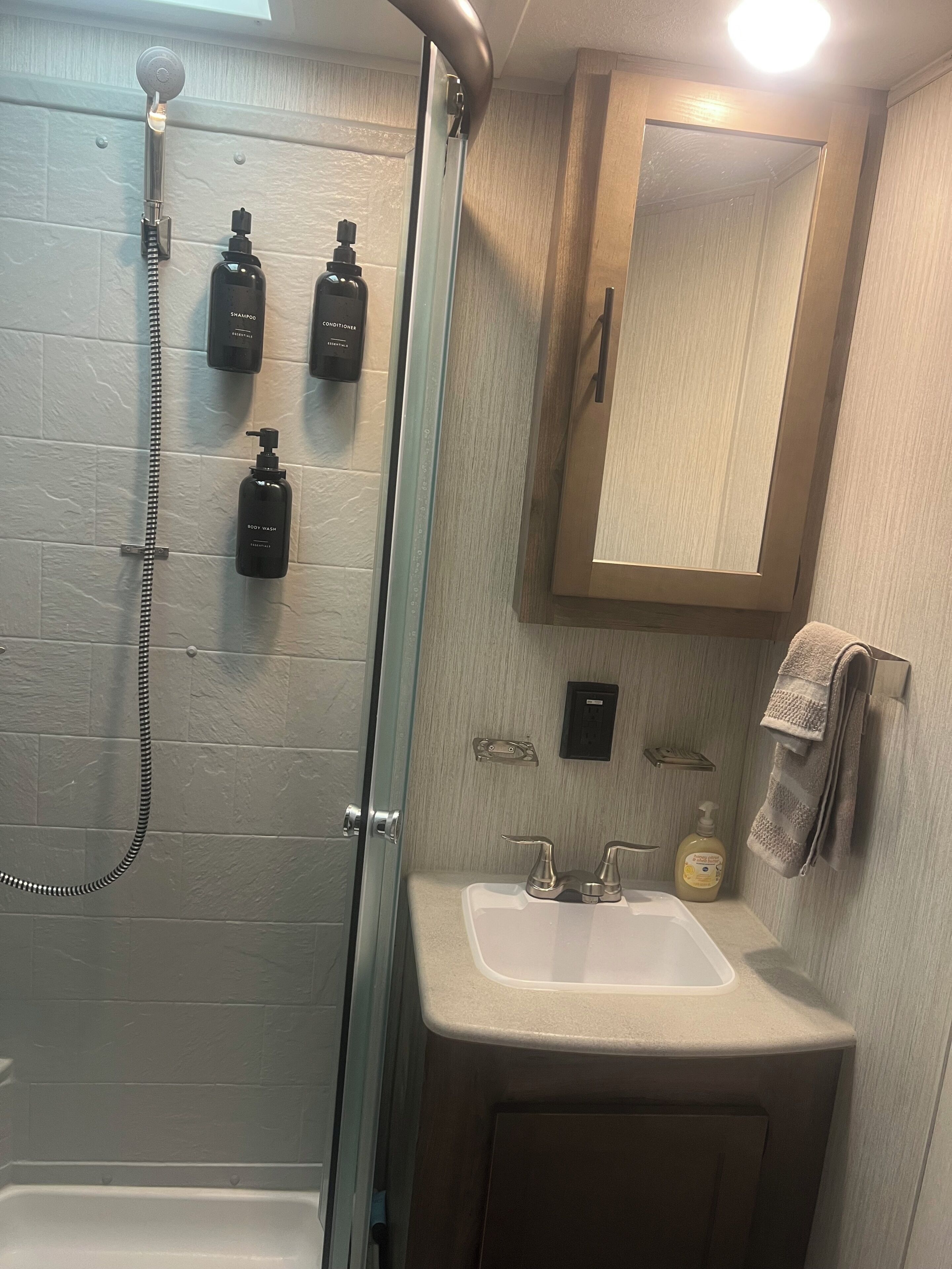 Une salle de bain avec une douche à parois de verre, un lavabo avec un miroir au-dessus et des articles de toilette fixés au mur.