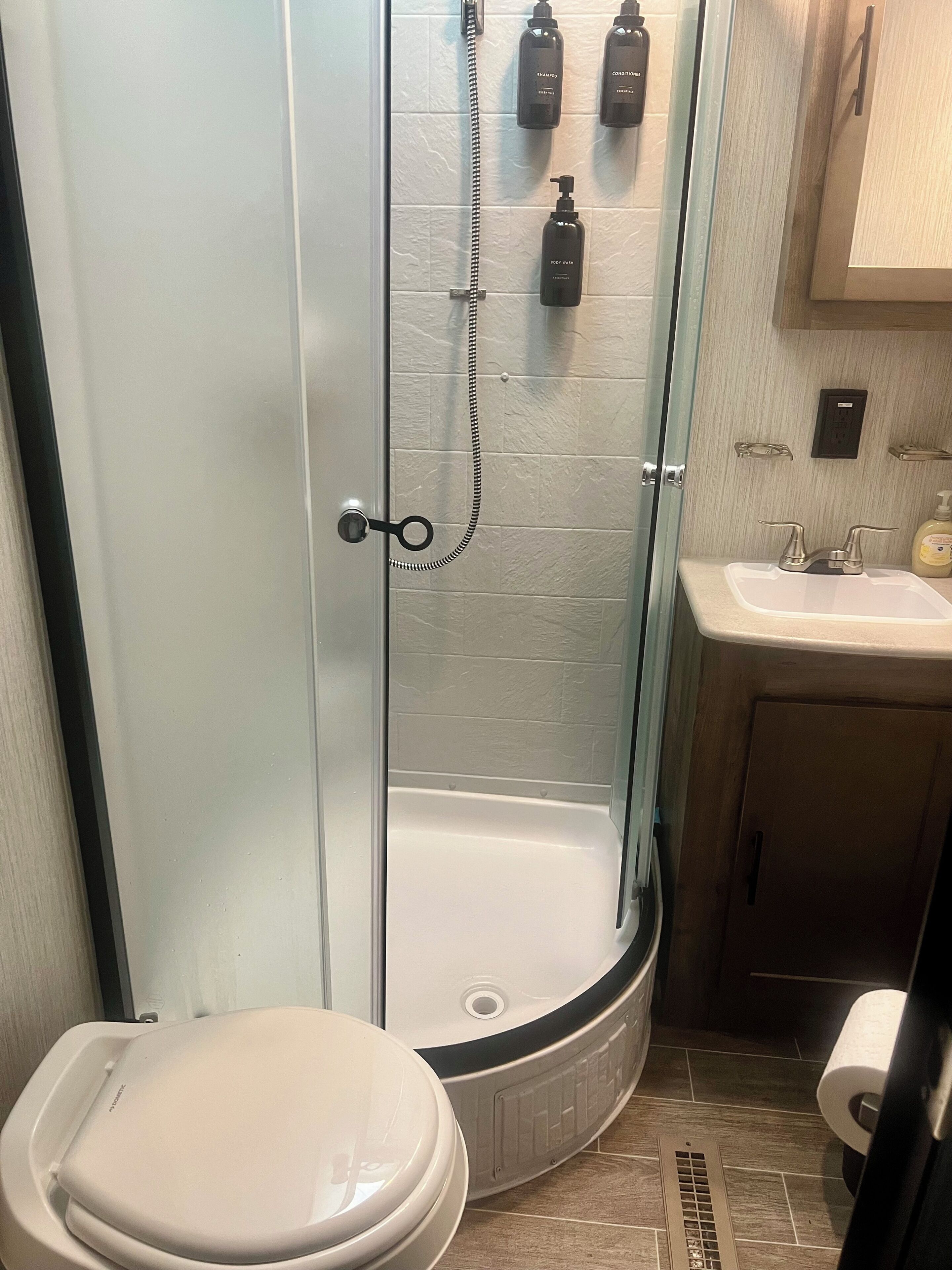 A bathroom with a glass-enclosed shower, a toilet, a sink, and toiletries on the wall.